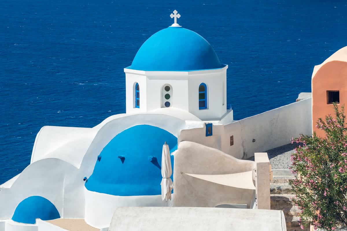 A whitewashed church with a blue dome above the sea